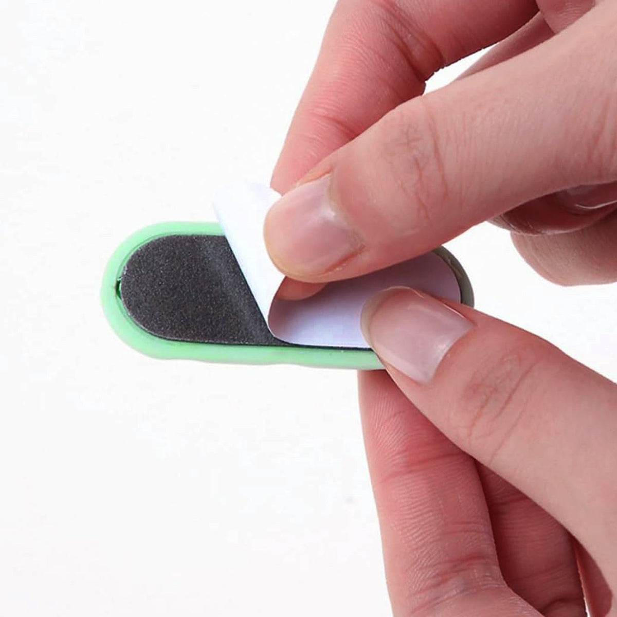Hands peel the adhesive backing off a green silicone cable organizer.