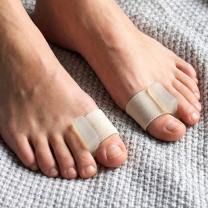 A close-up of two feet wearing beige elastic toe separators with clear gel pads, resting on a soft grey blanket.
