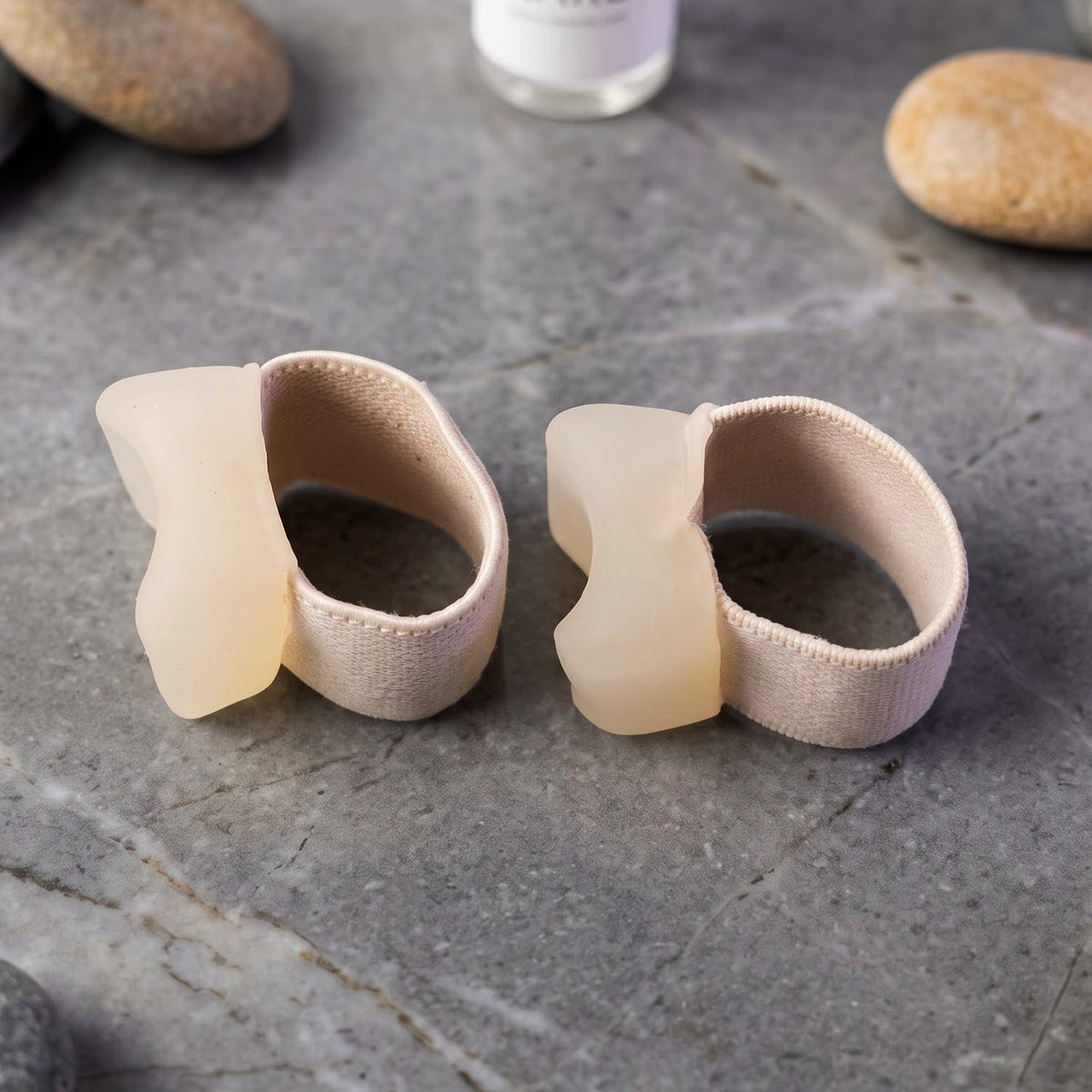 Two beige elastic toe separators with clear gel pads, viewed from the side, on a dark grey marble surface with decorative