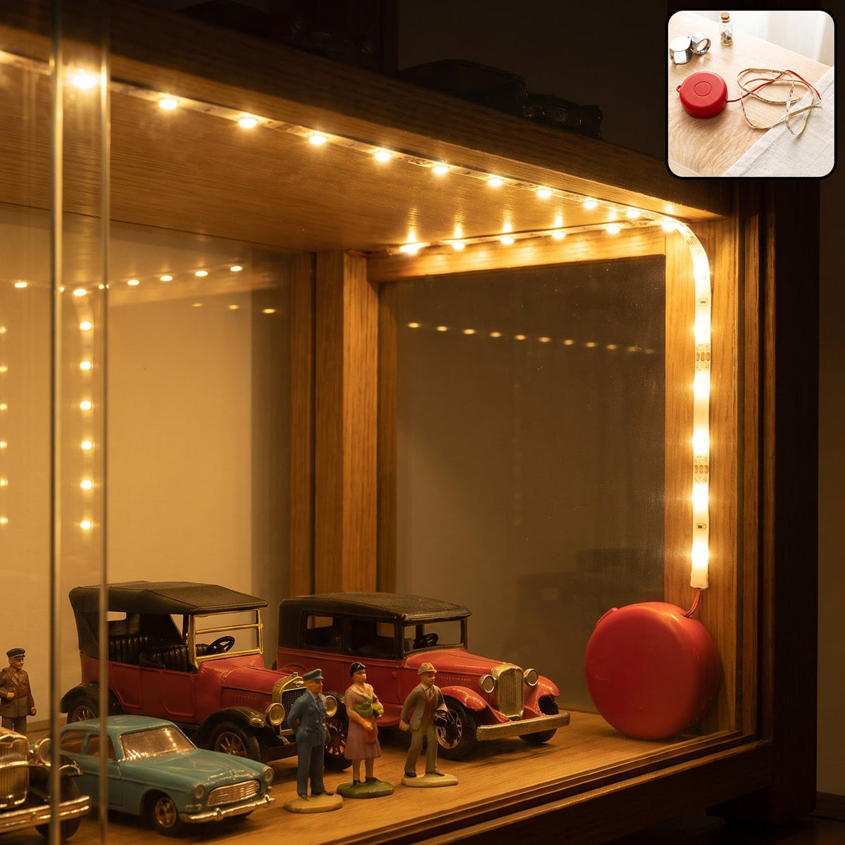 Warm white LED strip lights illuminate a wooden display cabinet with miniature vintage cars and figurines.