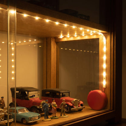 The illuminated LED strip lights provide ambient lighting for a collection of miniature cars in a wooden display case.
