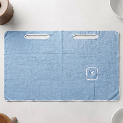 Flat lay of a light blue rectangular bath towel wrap with two armholes and a small pocket with an R monogram.