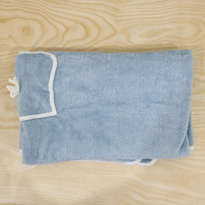 Folded light blue bath towel wrap with white trim and a small pocket, laid on a light wooden surface.