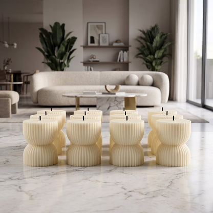 Twelve unlit, cream-colored, ribbed, hourglass-shaped LED candles stand on a light marble floor in a modern living space.