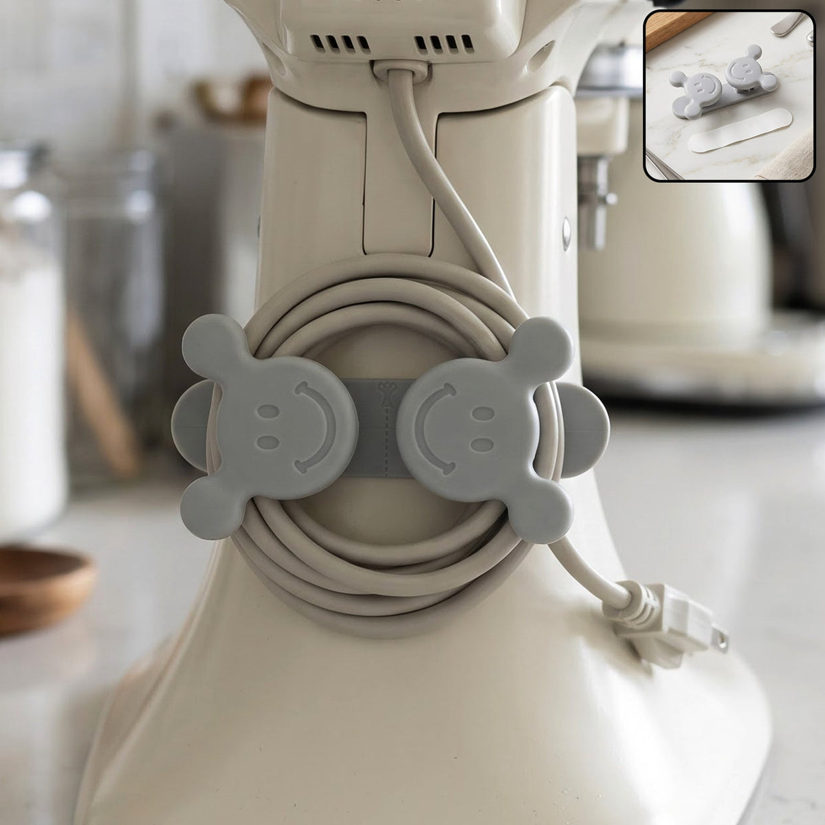 A gray silicone cord organizer with two smiling faces, holding a coiled light gray appliance cord on a white stand – view 3