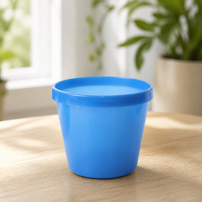A single blue plastic planter pot sits on a light wooden surface in a bright room.