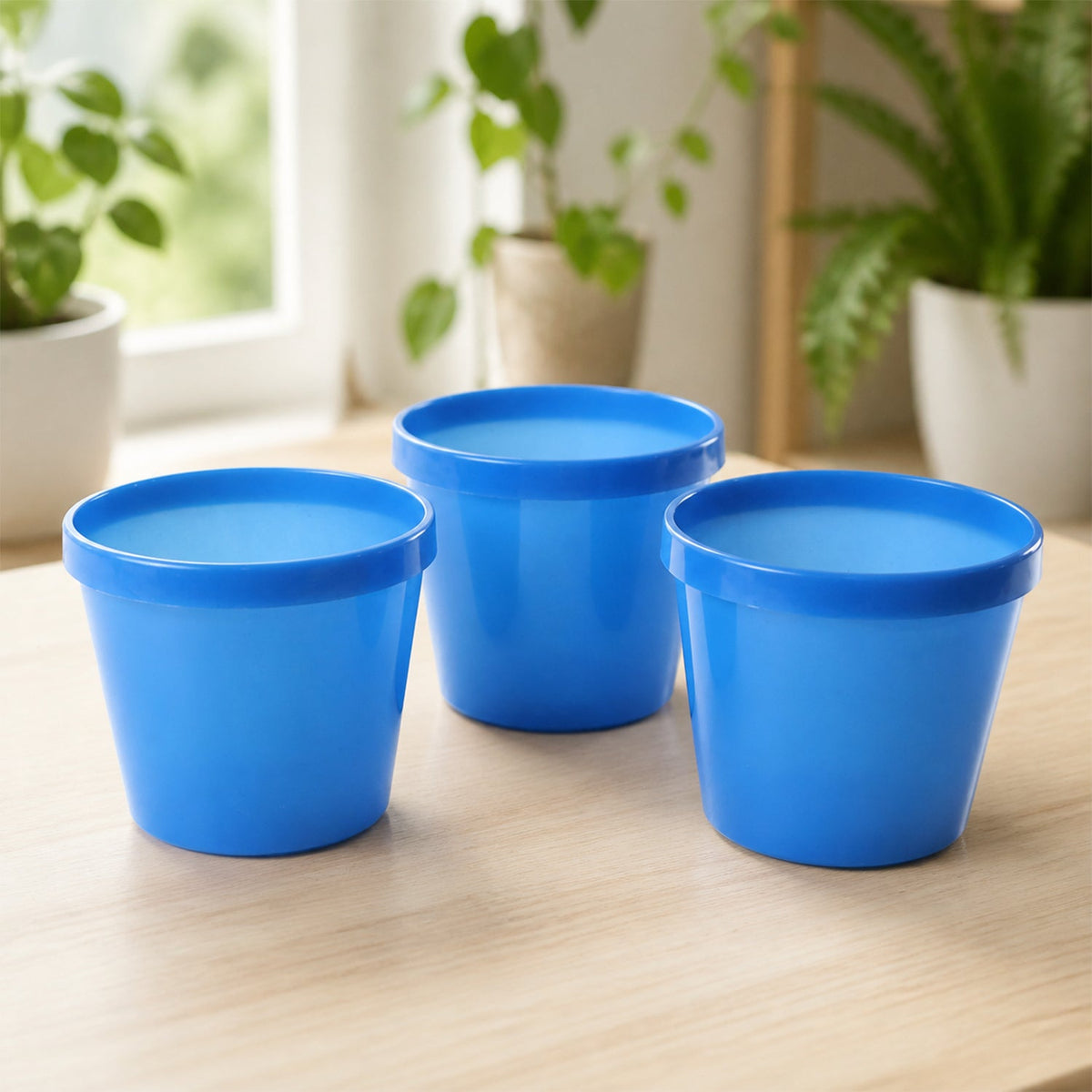 Three empty blue plastic planter pots are arranged on a light wooden table in a well-lit room.