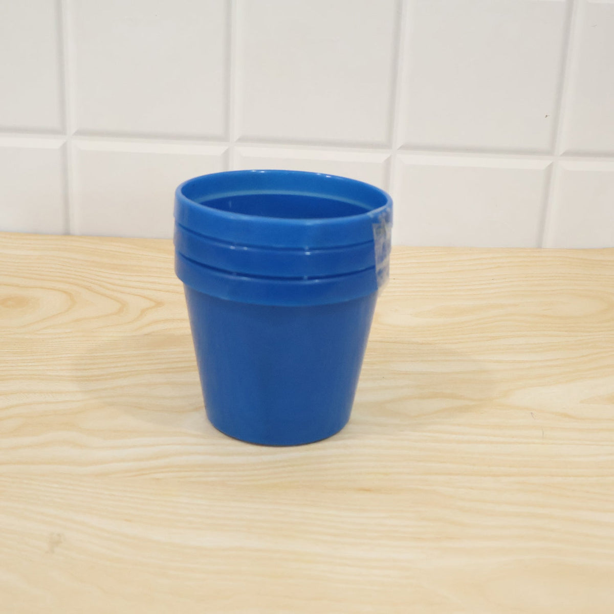 A stack of three blue plastic planter pots sits on a light wood surface against a tiled wall.