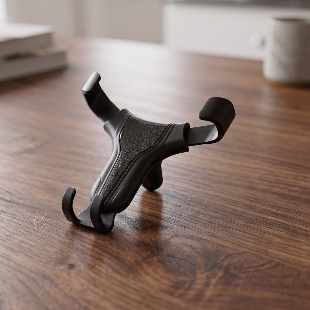 A black gravity lock car phone holder with textured grip pads resting on a light brown wooden desk.
