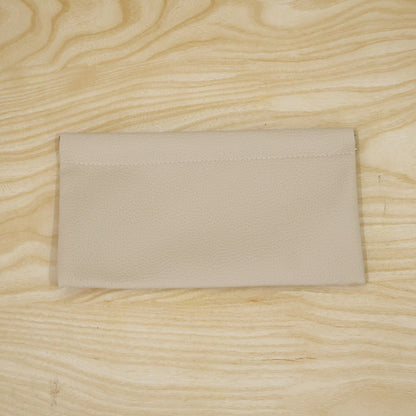 A cream textured faux leather pouch lying flat on a light wooden surface with visible grain.