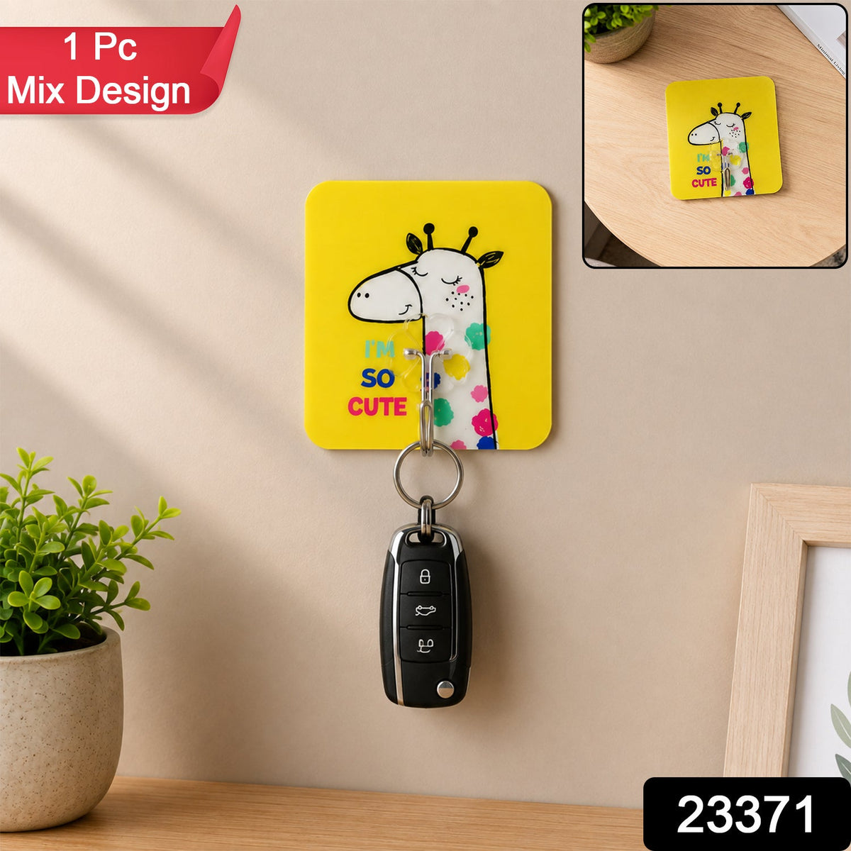 A yellow square wall hook with a cartoon giraffe and text "I'M SO CUTE" holds a black car key on a beige wall, with a small