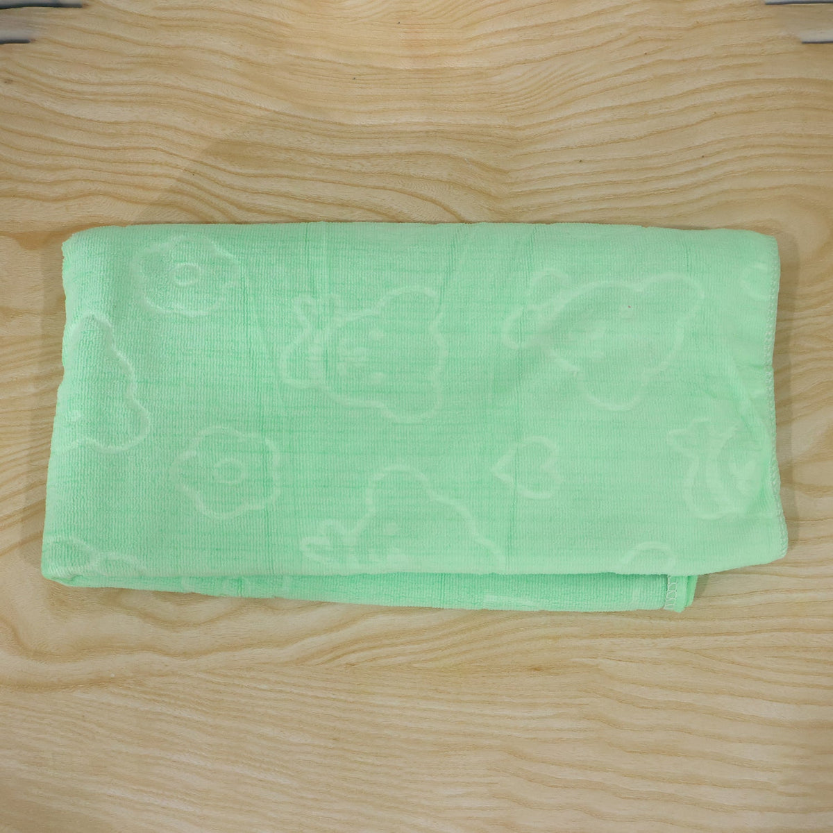 A light green microfiber towel with embossed heart and flower patterns, folded on a light wooden surface.