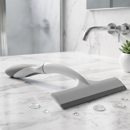 A white and gray glass wiper lying on a marble countertop with water droplets, next to a faucet.