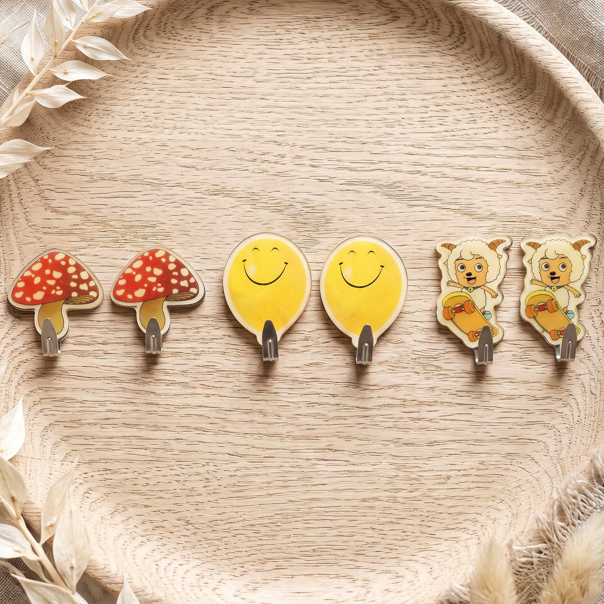 Six assorted cartoon wall hooks: two red mushrooms, two yellow smiling faces, and two sheep on skateboards, on a wooden tray.