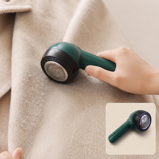 A hand holds a dark green and black lint remover against a light beige wool coat covered in small white lint balls.