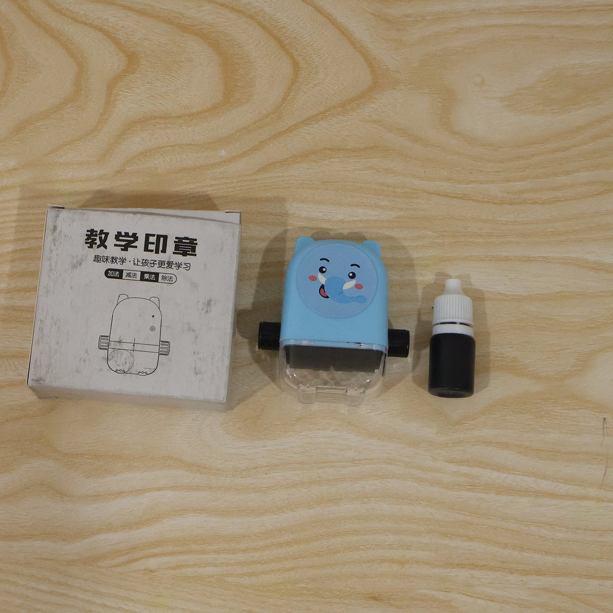 A blue elephant math roller stamp, a black ink bottle, and a white box with Chinese text and a stamp illustration are on a