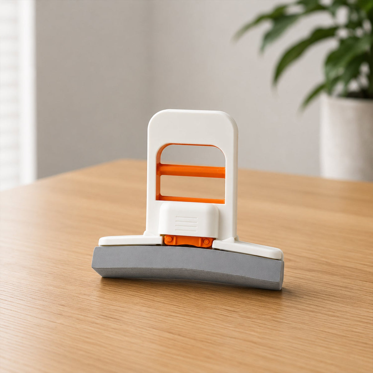 A hand uses a white and orange mini sponge mop to clean up a spilled coffee stain on a white desk next to a laptop.