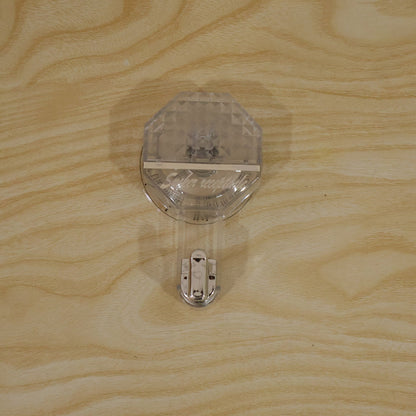 A clear, diamond-patterned self-adhesive hook with a silver hook, attached to a light wooden surface.
