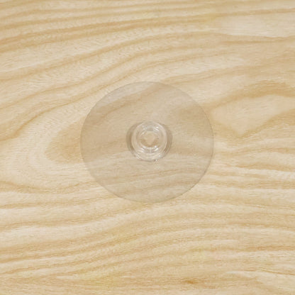 A clear plastic suction cup hook is centered on a light brown wooden surface with visible grain.