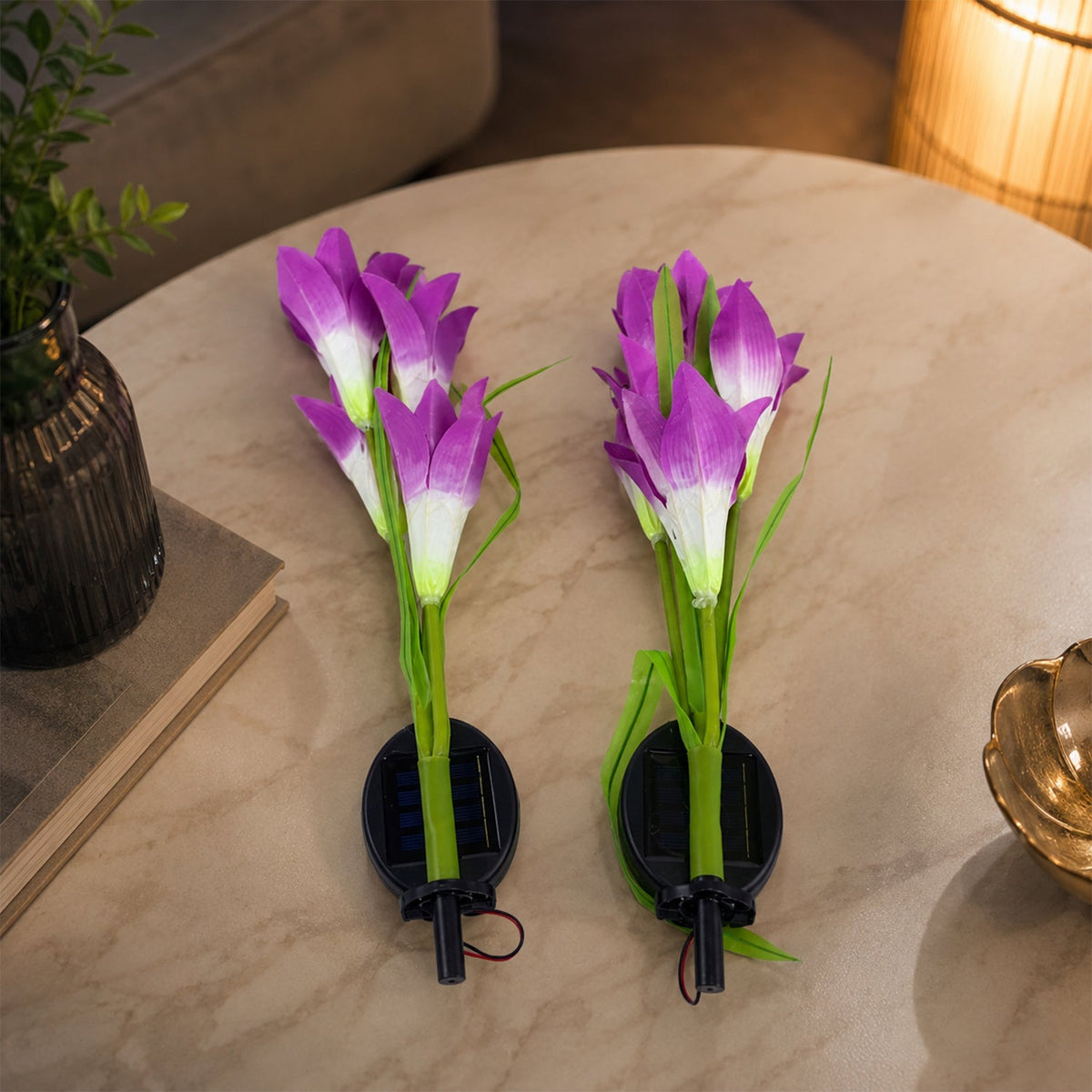 Two purple and white solar flower stake lights with attached solar panels rest on a light-colored table indoors.
