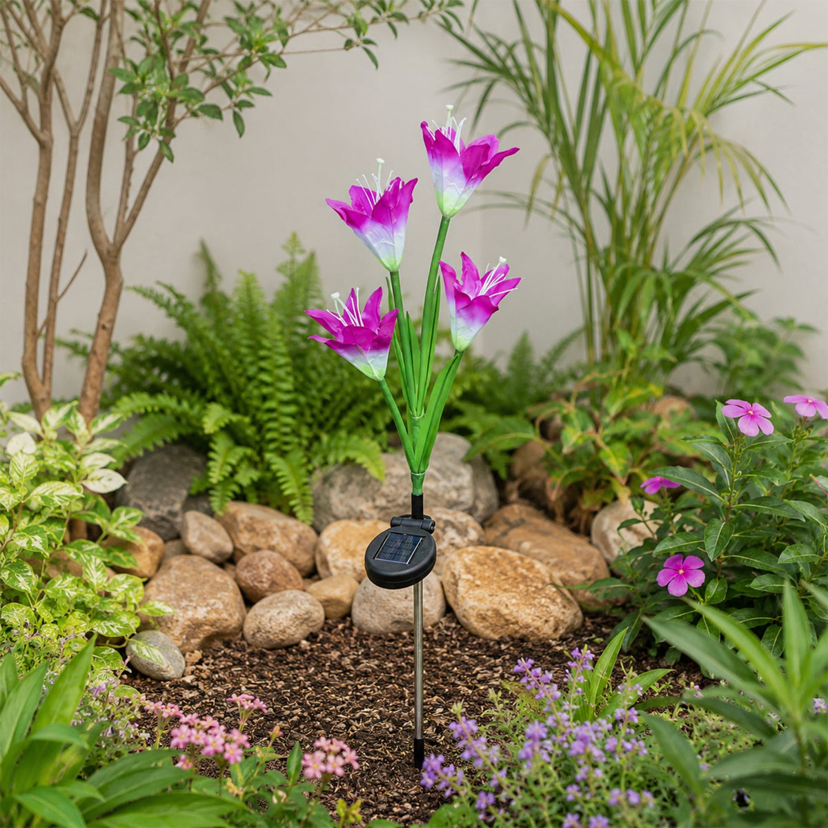 A purple and white solar flower stake light is planted in a landscaped garden bed with rocks and green plants.