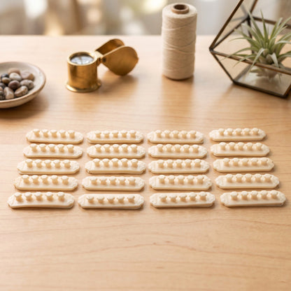 Twenty beige self-adhesive cable organizer clips, each with five flower-shaped holders, arranged on a light wooden table