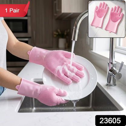 Hands wearing pink silicone gloves with scrubbing bristles washing a white plate under running water in a kitchen sink, with
