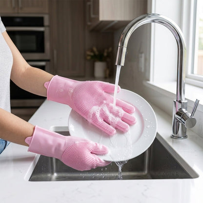 Hands wearing pink silicone gloves with scrubbing bristles washing a white plate under running water in a modern kitchen