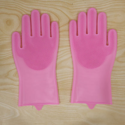 A pair of pink silicone scrubbing gloves with textured palms laid flat on a light wooden surface.