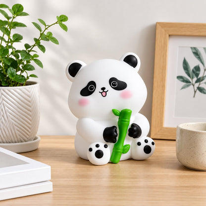 White panda night light with black details and pink cheeks, holding a green bamboo stalk, on a light wooden desk with a
