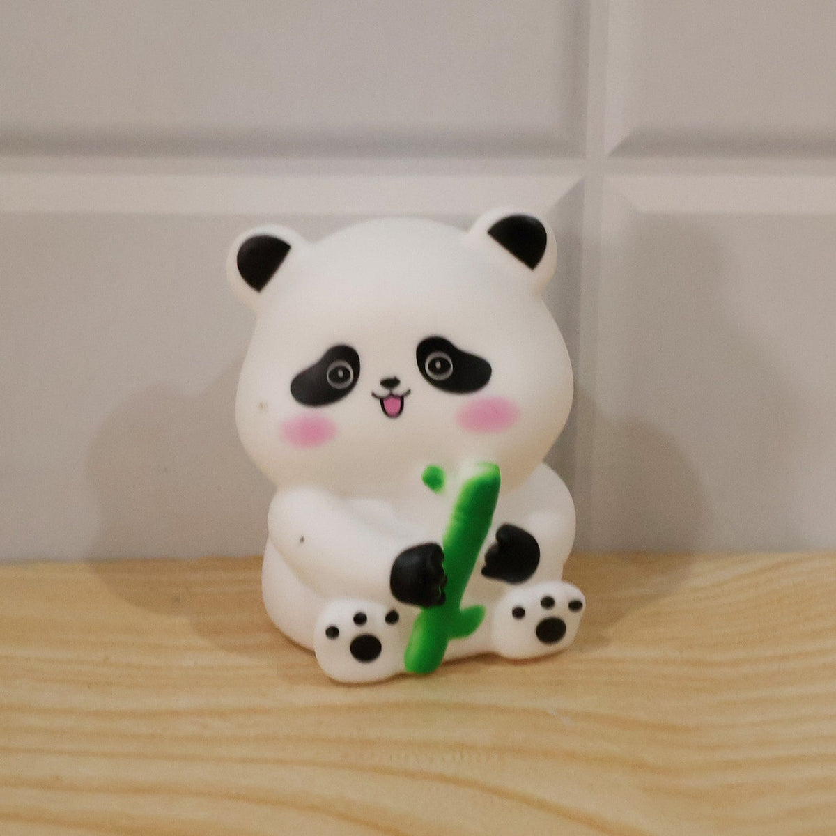 Simple front view of the white panda night light with black ears, eyes, and paws, holding a green bamboo, on a wooden