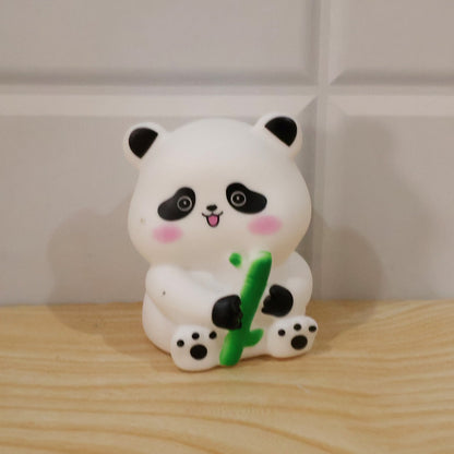 Simple front view of the white panda night light with black ears, eyes, and paws, holding a green bamboo, on a wooden