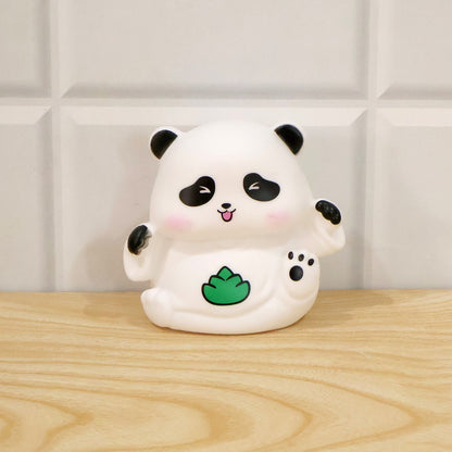 A white panda night light with black details and a green leaf, sitting on a light wooden surface.