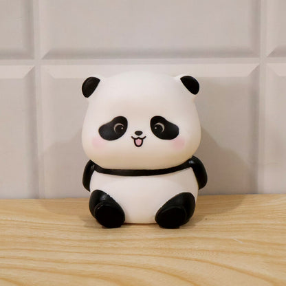 A panda night light with black features on a wooden surface against a white tiled wall.