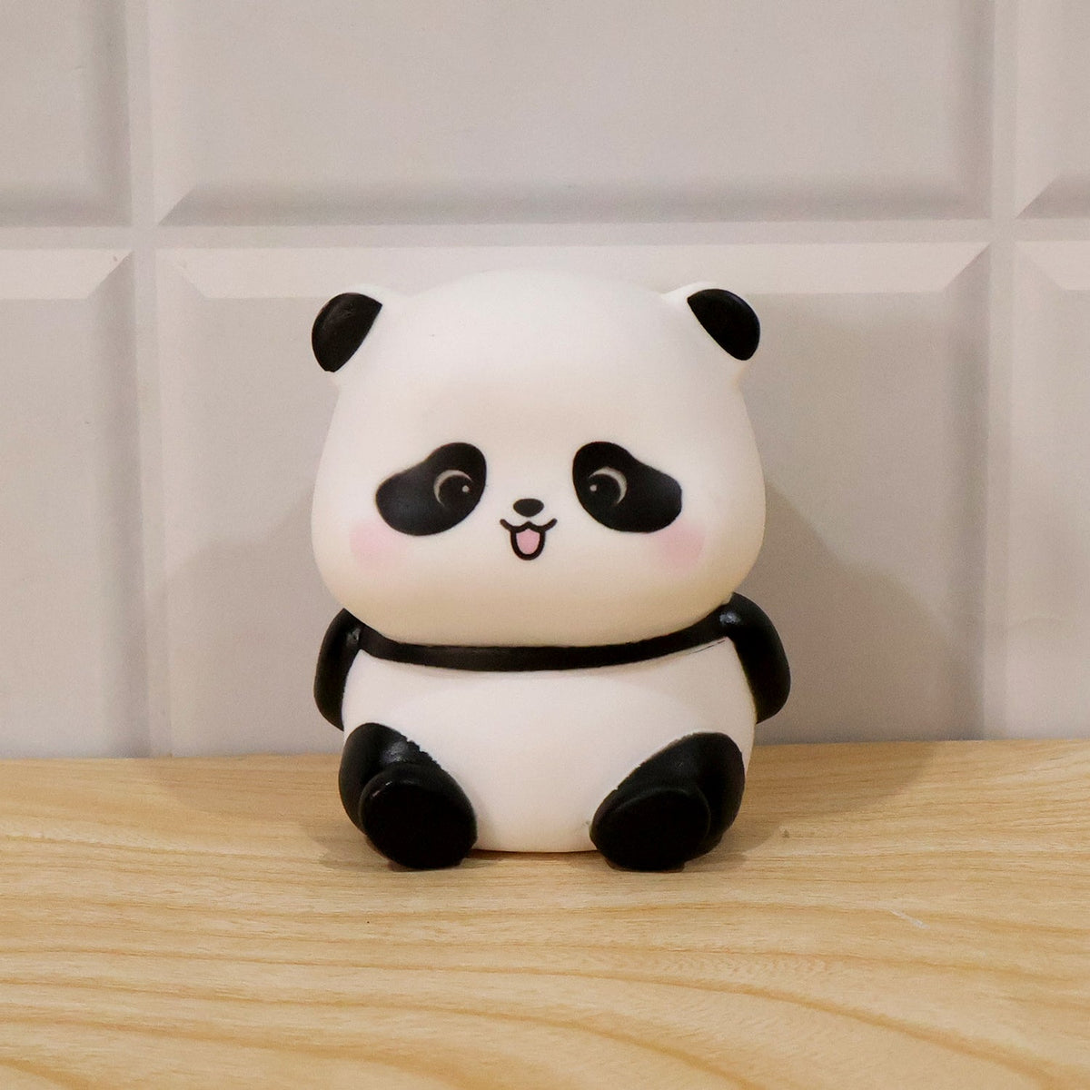 A panda night light with black features on a wooden surface against a white tiled wall.