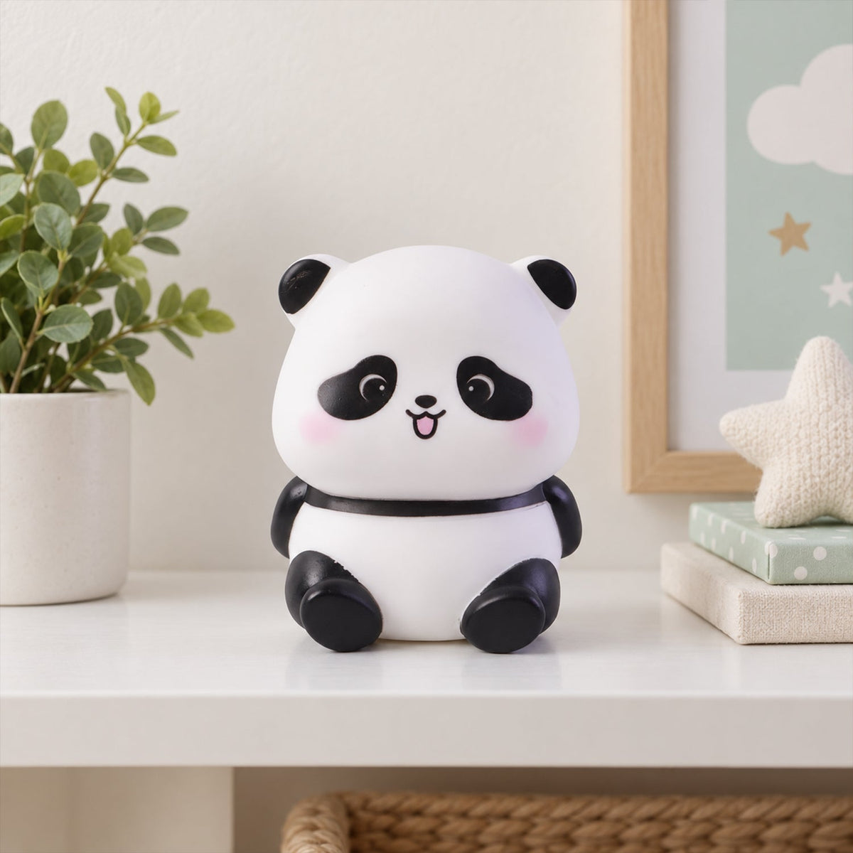 An unlit panda night light sits on a white shelf with a potted plant and framed artwork in the background.