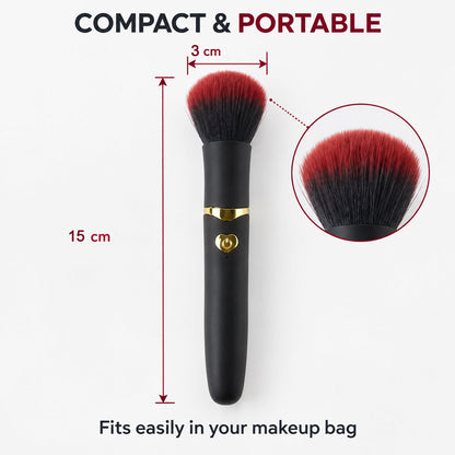 A black and red makeup brush with gold accents stands on a vanity table with blurred perfumes and a mirror in the background.