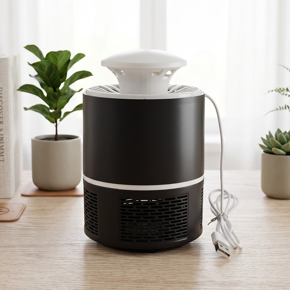 Black and white mosquito killer lamp with its USB cable coiled on a wooden desk with plants and books.