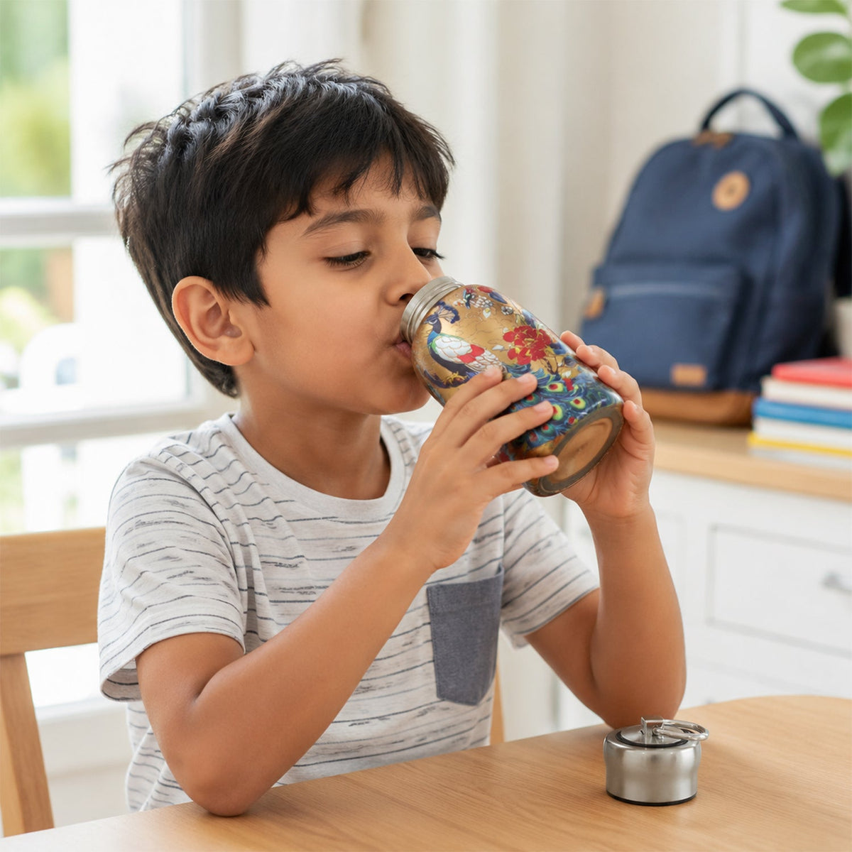 A young boy drinking from the golden stainless steel vacuum bottle with a peacock and floral print.