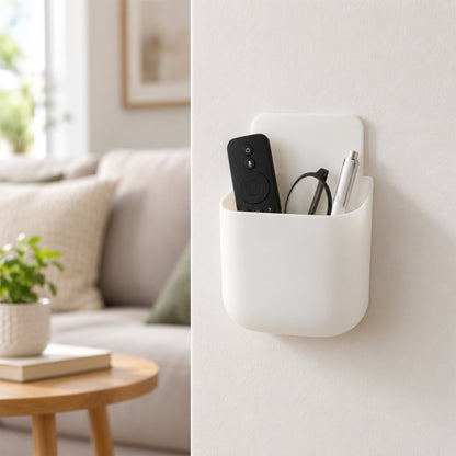 White adhesive organizer mounted on a wall, holding a black remote, glasses, and a silver pen.