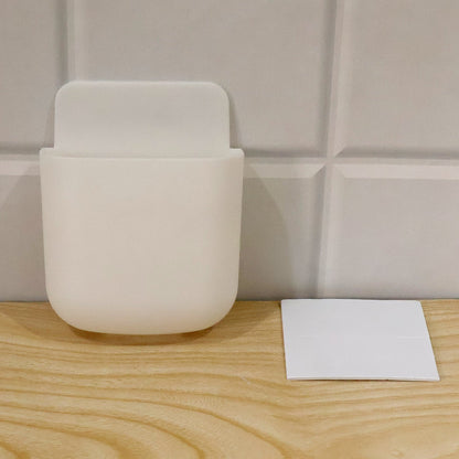 White adhesive organizer on a wooden surface next to a white adhesive pad, against a tiled wall.