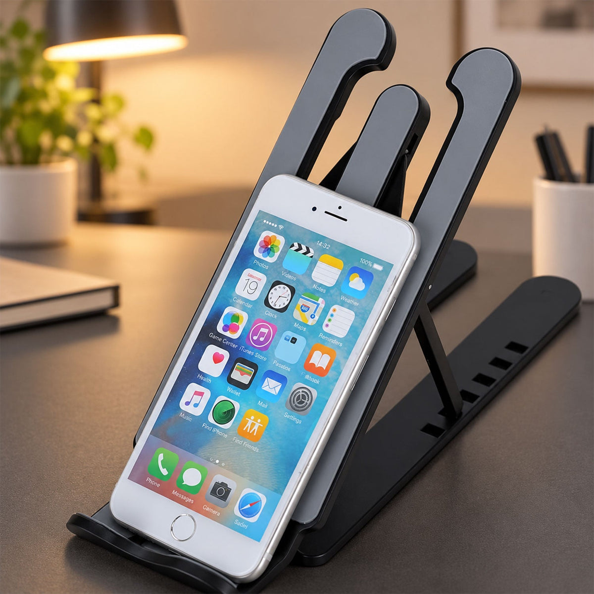 A white smartphone is cradled in the black and gray adjustable stand on a dark gray desk.