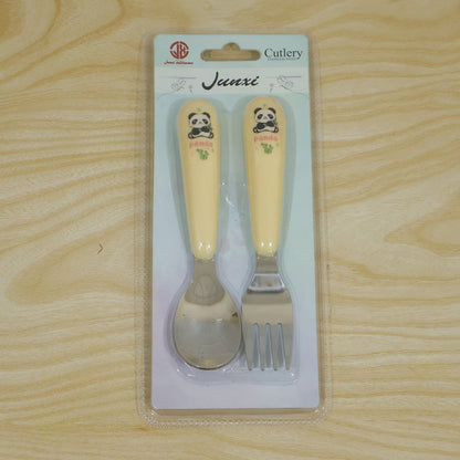 A yellow and silver panda-themed spoon and fork set is sealed in clear plastic packaging on a light wooden surface.