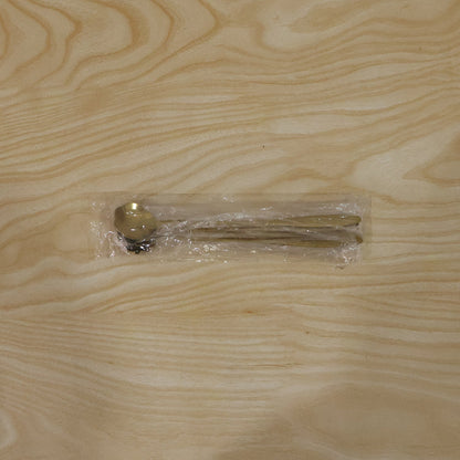 Three gold spoons are sealed in clear plastic packaging on a light wooden surface.