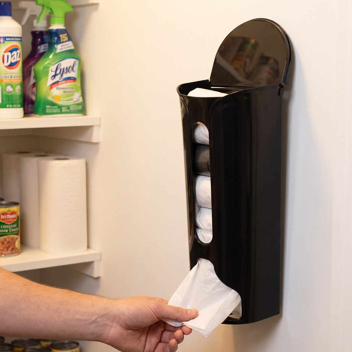A hand pulls a white plastic bag from the bottom of a black wall-mounted dispenser, full of bags. – view 3