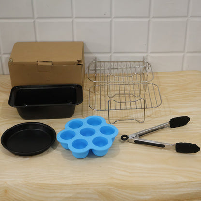 A complete set of air fryer accessories on a light wooden surface, including a cardboard box, two metal racks, a black loaf