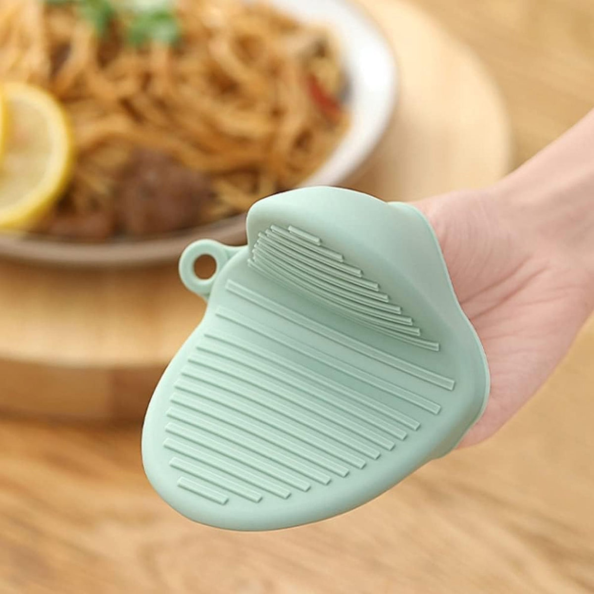 Close-up of a hand holding a green silicone mini oven mitt with textured grip lines.