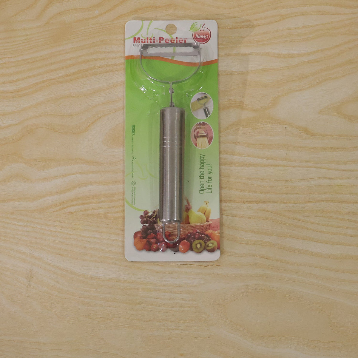 A stainless steel peeler in its retail packaging, labeled 'Multi-Peeler', resting on a light wooden surface.