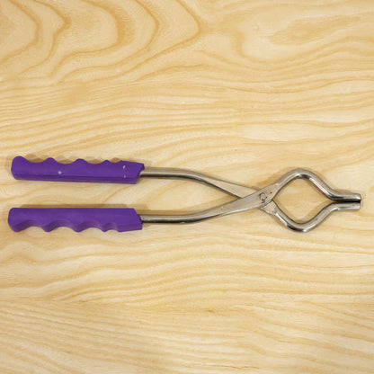 A stainless steel pot lifter with purple handles lying on a light wooden surface.