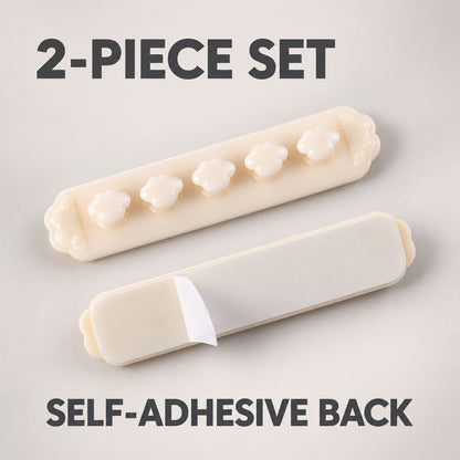 Two beige flower-shaped cable organizer clips, one with the self-adhesive backing partially peeled off, on a light grey